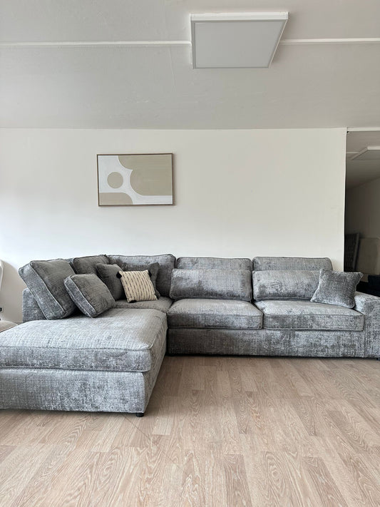 Canapé d'angle Lexus Marbella beige de la marque HomeDeLuxe, avec coussins confortables et revêtement en tissu dans un salon moderne.