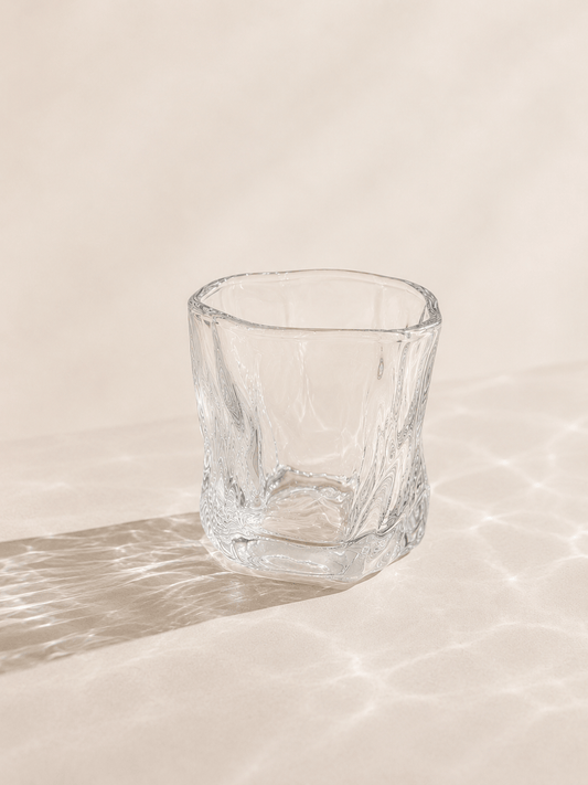 Douze petits verres à eau en verre transparent de la marque HomeDeLuxe, alignés sur une surface blanche.