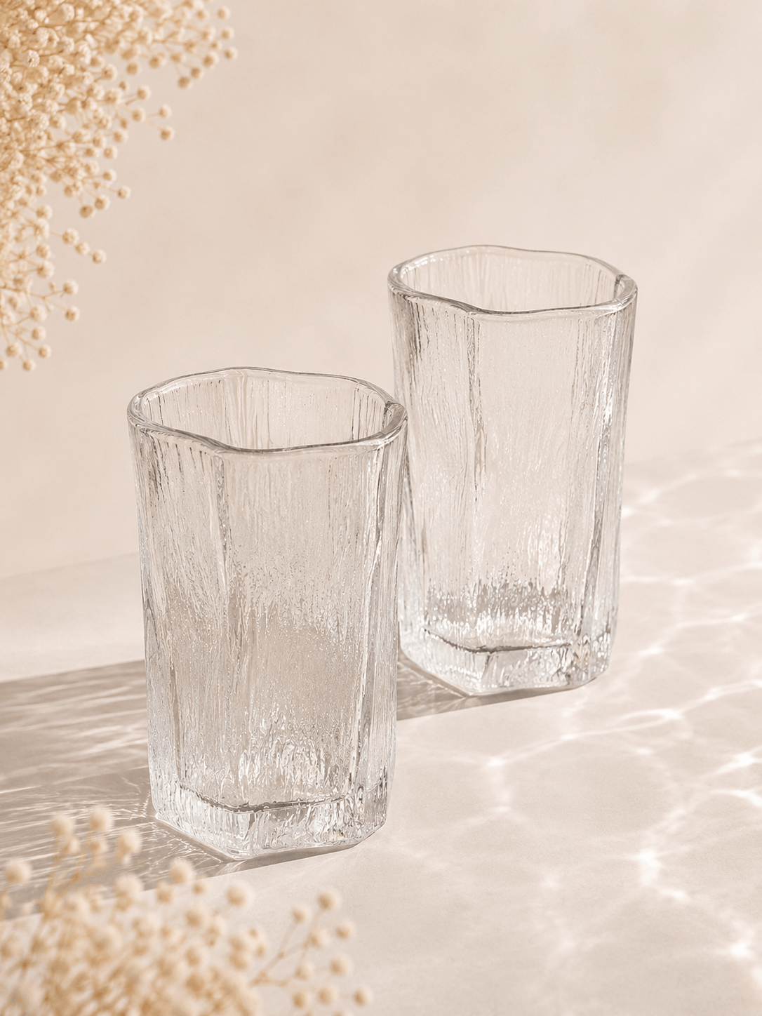 Douze verres à eau en verre clair de la marque HomeDeLuxe, design élégant, disposés sur une table.