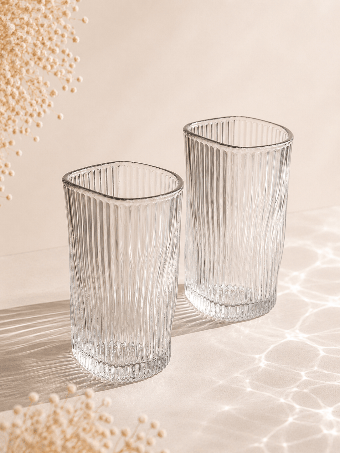 Douze verres à eau en verre transparent de la marque HomeDeLuxe, design élégant et moderne, disposés sur une surface.