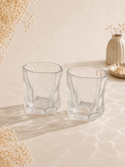 Douze petits verres à eau en verre transparent de la marque HomeDeLuxe, disposés sur une table.